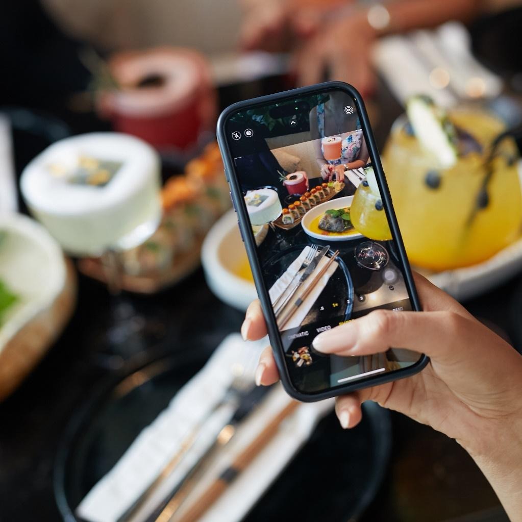 A woman taking a picture of food and drinks on her mobile phone